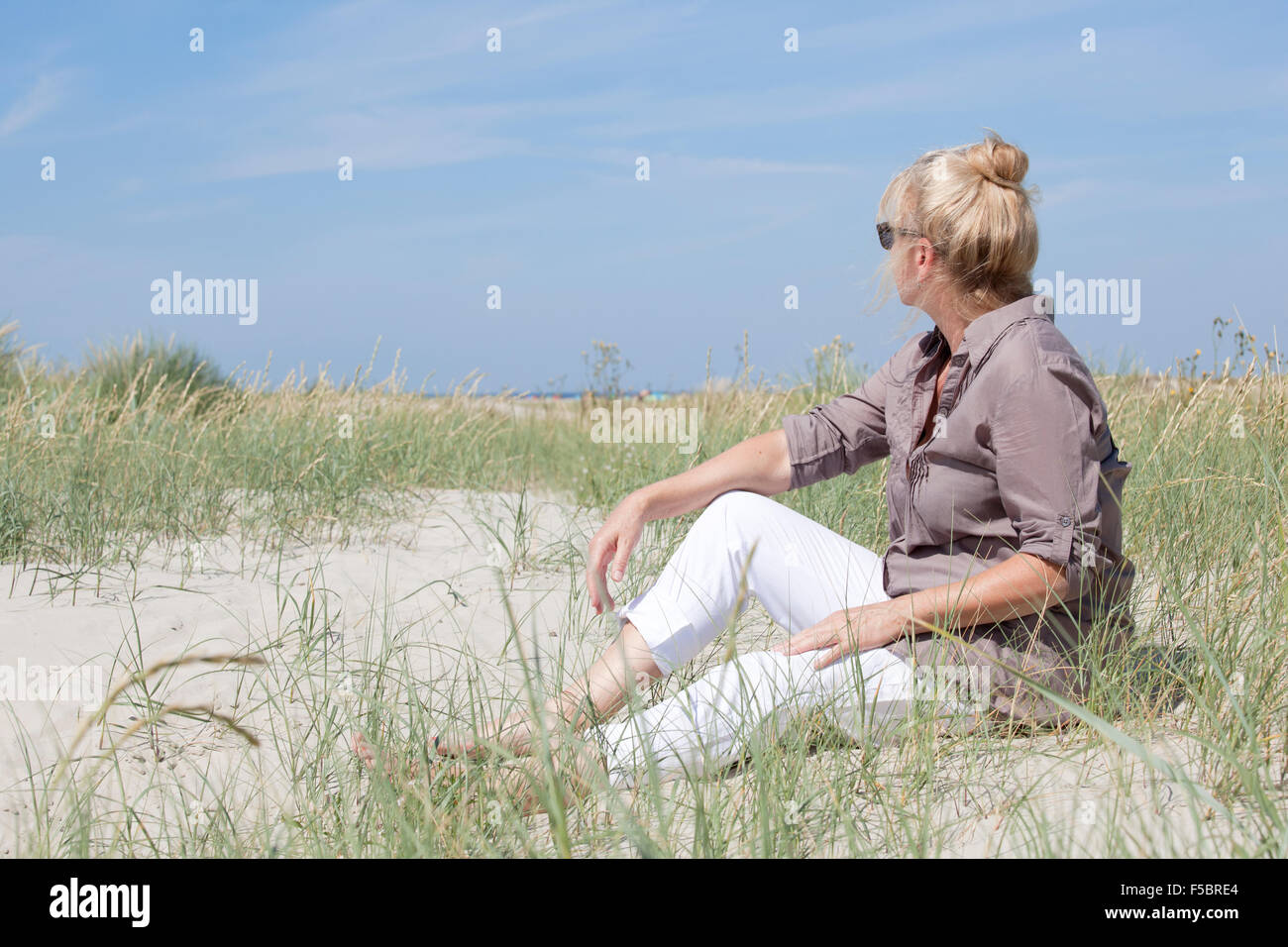 Ein Senior Frau sitzt in den Dünen auf einem Strand und schaut in die Ferne Stockfoto