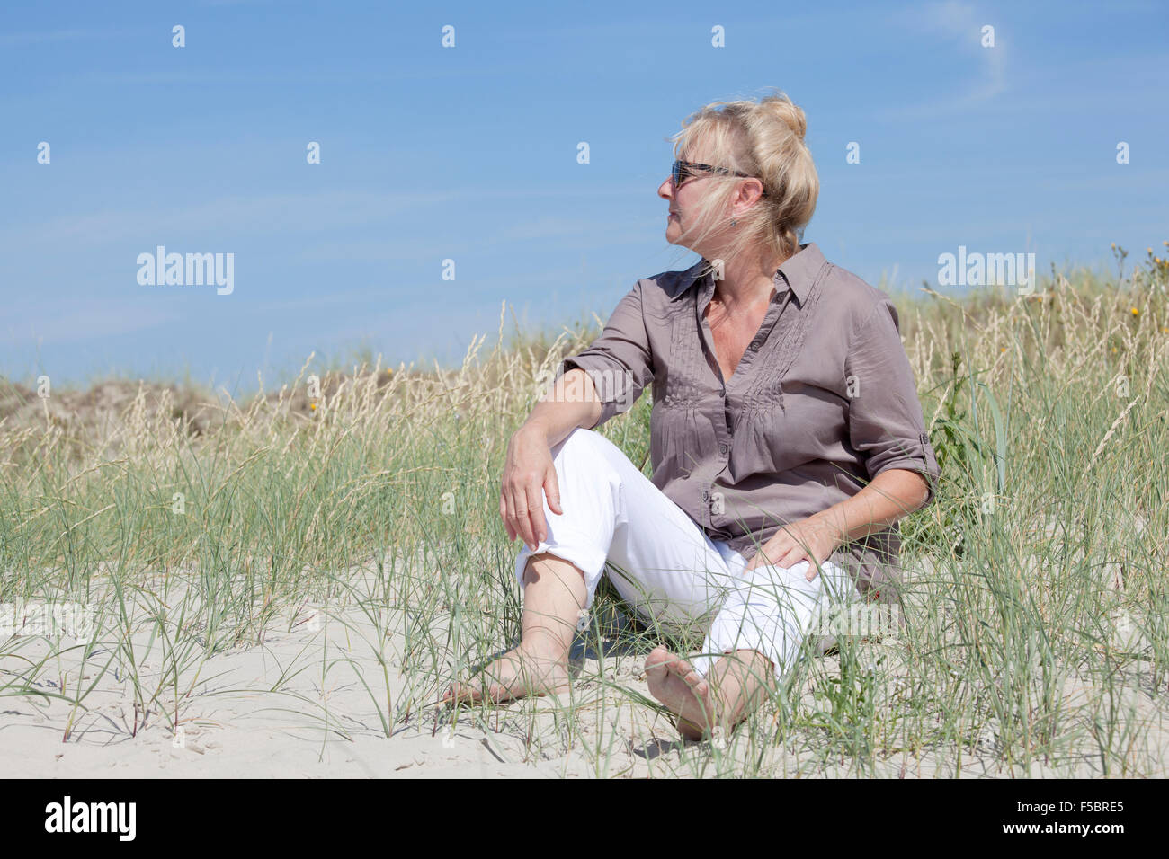 Ein Senior Frau sitzt in den Dünen auf einem Strand und schaut in die Ferne Stockfoto