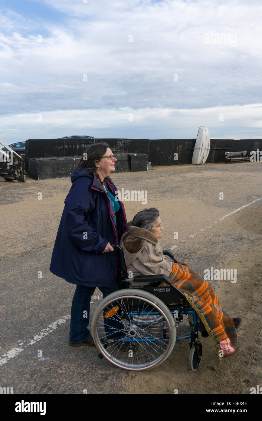 Eine 95 Jahre alte Frau mit ihrem Betreuer oder Helfer auf der Mole in Broadstairs, gut verpackt gegen die Kälte an einem strahlenden Herbsttag. Stockfoto