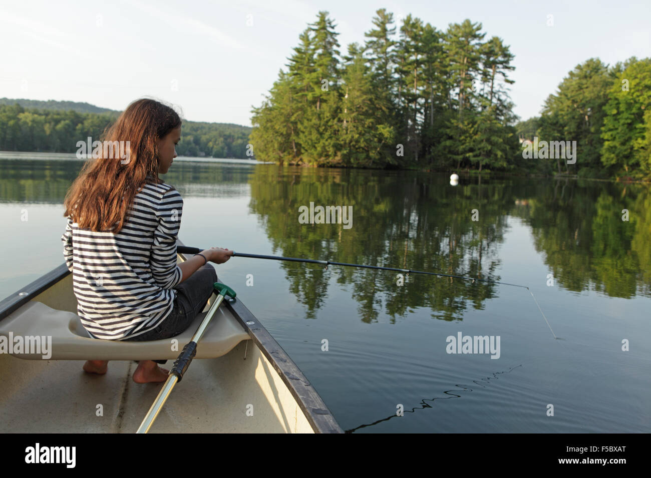 Junges Mädchen Angeln vom Kanu auf einem ruhigen See mit Bäumen im Hintergrund Stockfoto