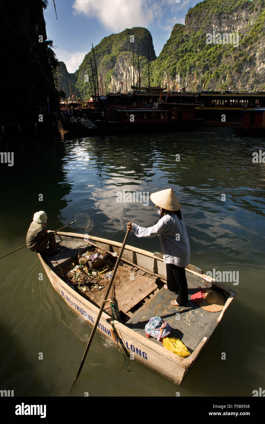 Frau Rudern, sammeln Müll von Touristenbooten, Halong Bucht, Vietnam. Rudern durch Halong Bucht, Vietnam. Katze Stockfoto