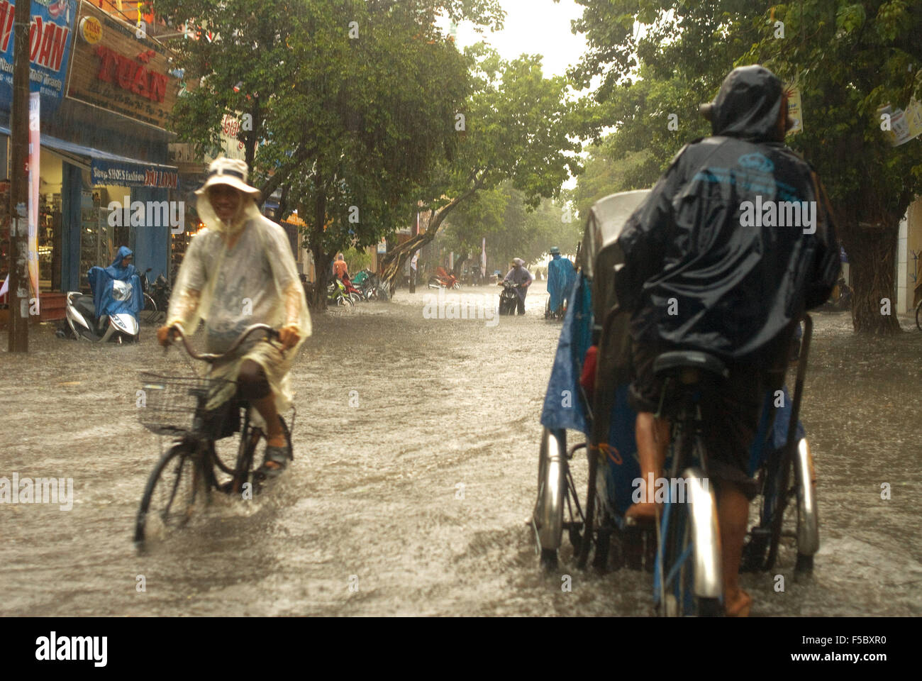 Monsunregen in der Stadt Hue. Menschen in Tuc-Tuc-Fahrten mit dem Fahrrad entlang überfluteten Straßen in Hue. Vietnam. Stockfoto