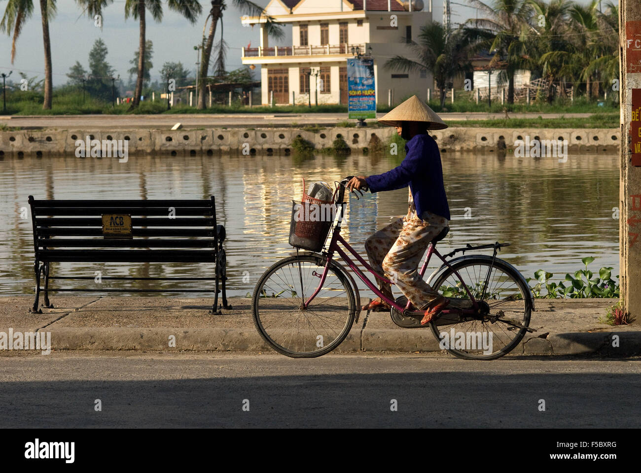 Radfahrer-Frau auf der Promenade am Thu Bon Fluss in Hoi An Vietnam. Typischen Vietnamesischen Frau mit Hut. Stockfoto