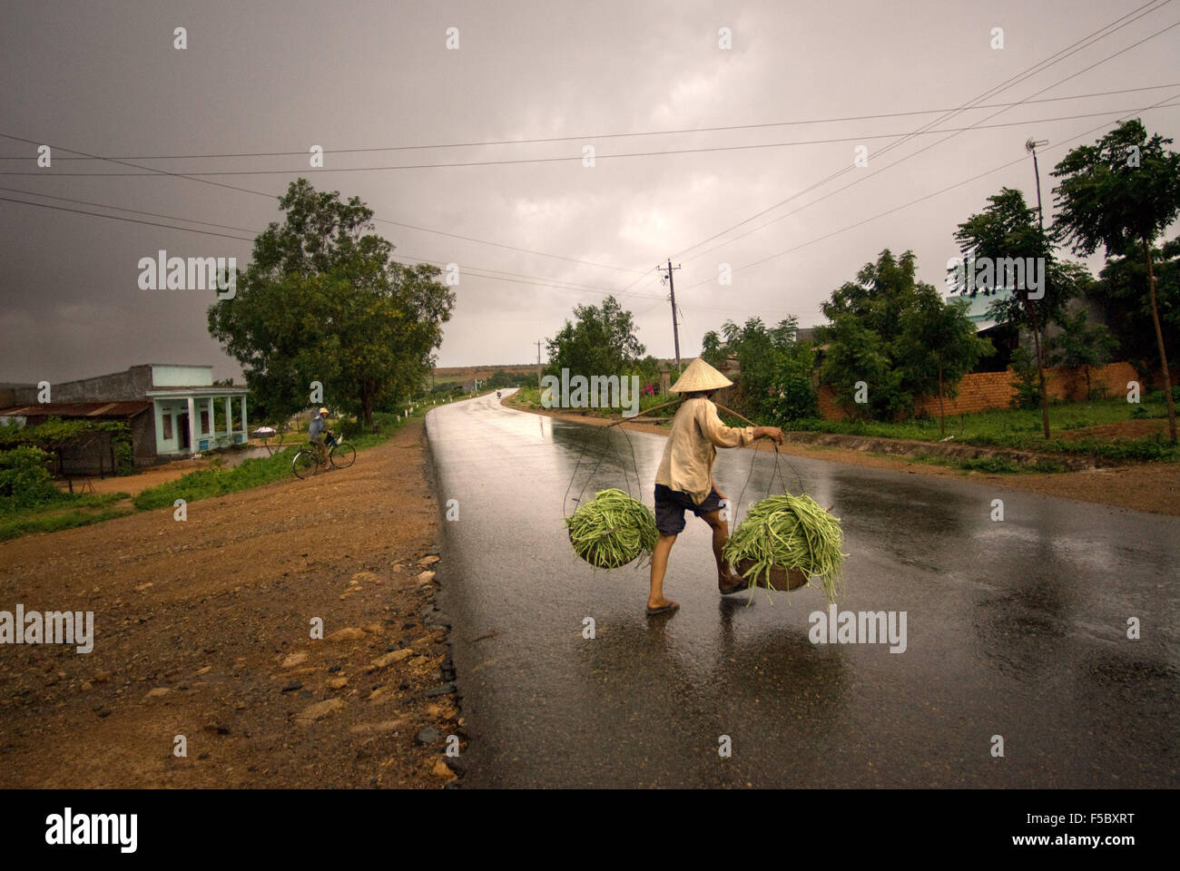 Eine Frau kehrt in das Feld nach einem Regen auf einer Straße am Stadtrand von Mui Ne. Vietnam. Stockfoto