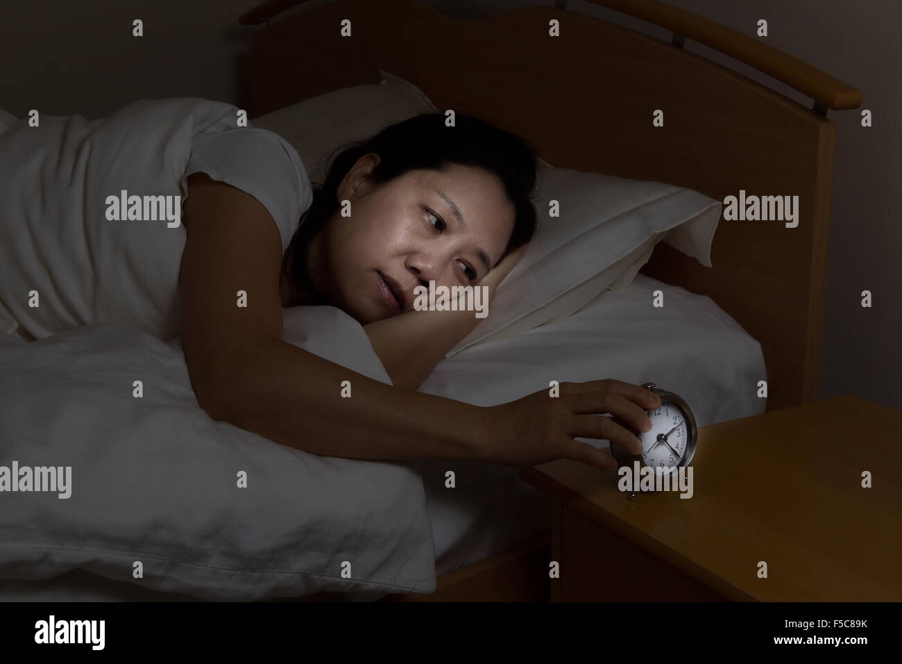 Frau mit Schlaflosigkeit Wecker zu berühren, während die Augen öffnen. Wählen Sie Licht und Fokus auf Frau und Uhr mit dunkler Hintergrund Stockfoto