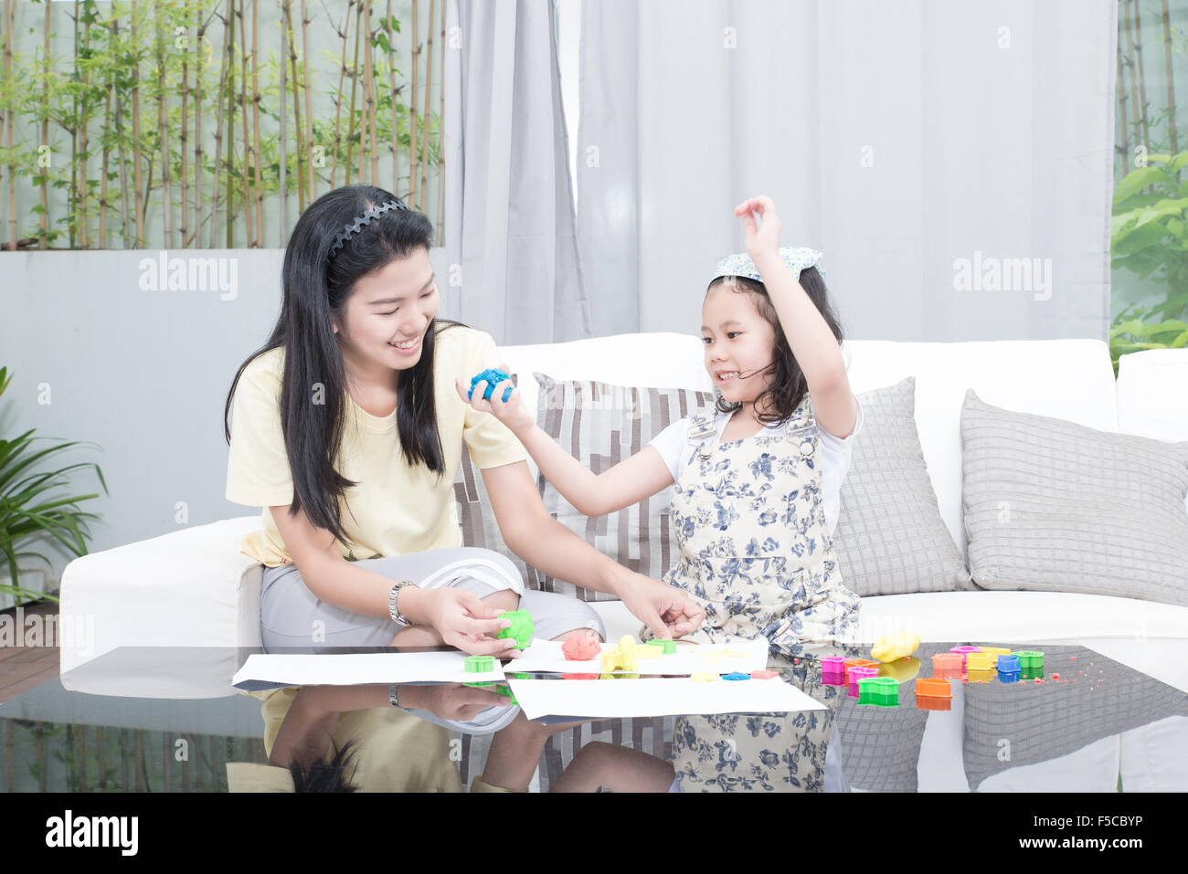 Familie, Kinder und glückliche Menschen Konzept - asiatische Mutter und Kind Tochter spielt mit Plastilin in Haus Stockfoto