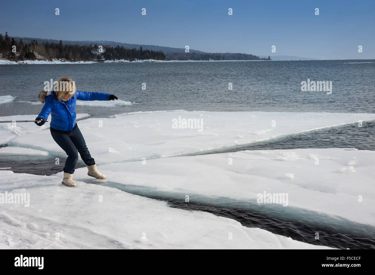 Erwachsenen blonde Frau trägt einen Mantel und Stiefel behutsam Schritte auf einer riesigen Eisscholle schweben am Lake Superior Stockfoto