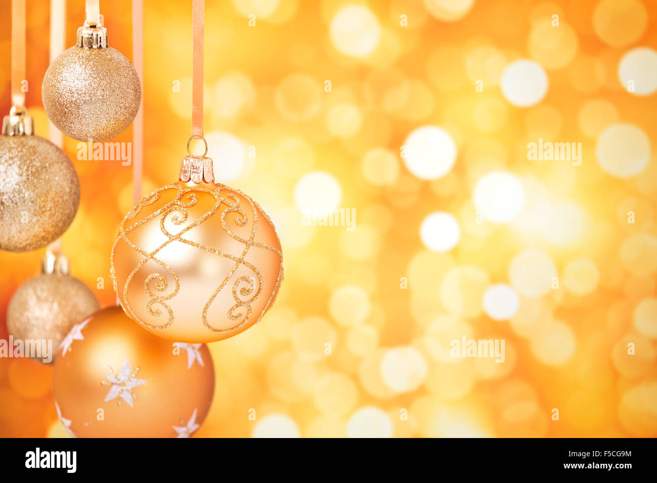 Goldene Weihnachtskugeln hängen vor defokussierten goldenen Lichter. Stockfoto
