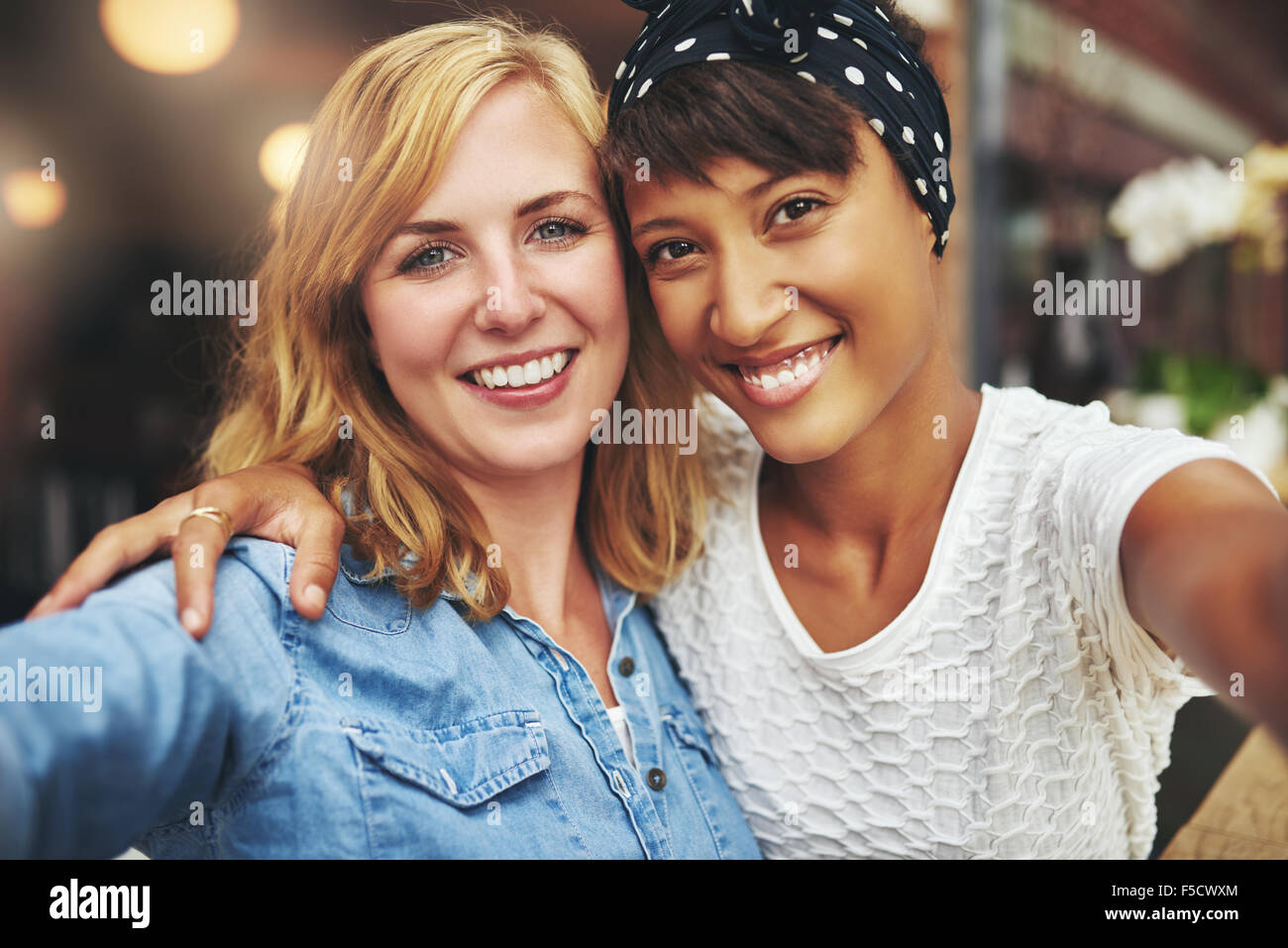 Zwei beste Freundinnen, die jungen Frauen Arm in Arm mit ihren Gesichtern sitzen schließen zusammen lächelnd in die Kamera, multiethnischen paar Stockfoto