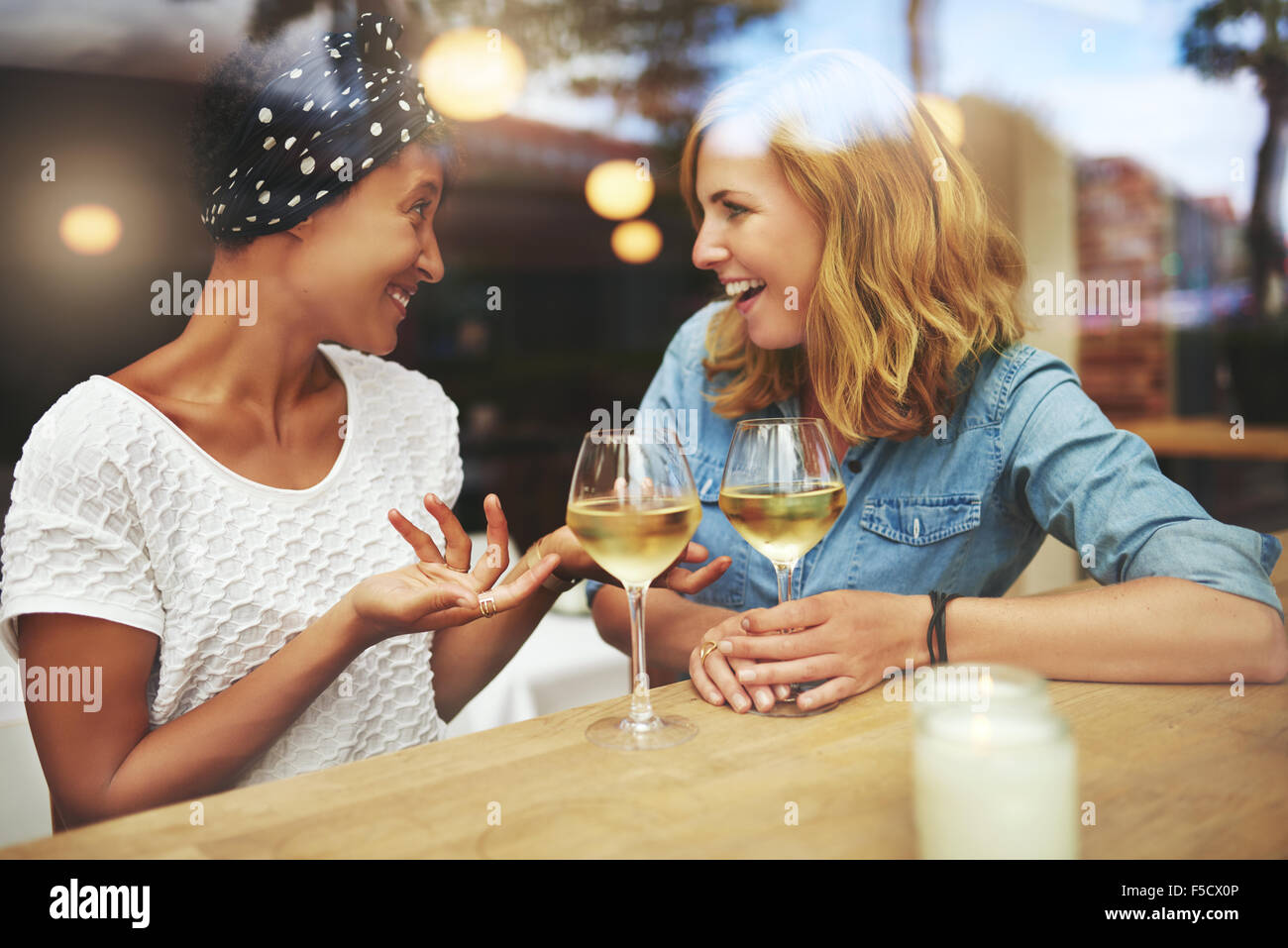 Zwei attraktive Frauen genießen ein Glas Wein zusammen in einer Kneipe sitzt an einem Tisch, lachen und plaudern mit Reflexionen Stockfoto