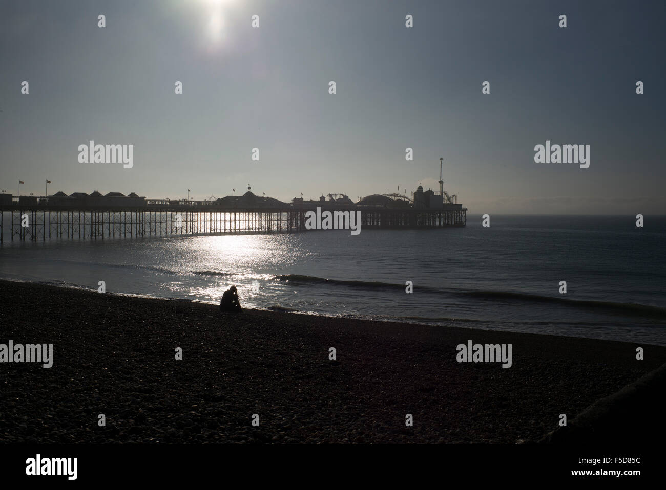 Einsame Figur sitzt am Strand vor Palace Pier von Brighton, am frühen Morgen. Stockfoto