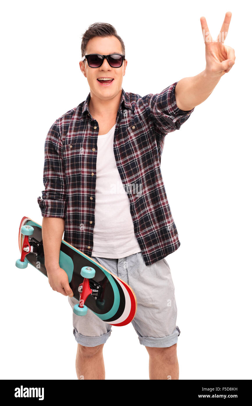 Vertikale Schuss eine junge männliche Skater hält eine Skateboard und ein Frieden Hand Geste isoliert auf weißem Hintergrund Stockfoto