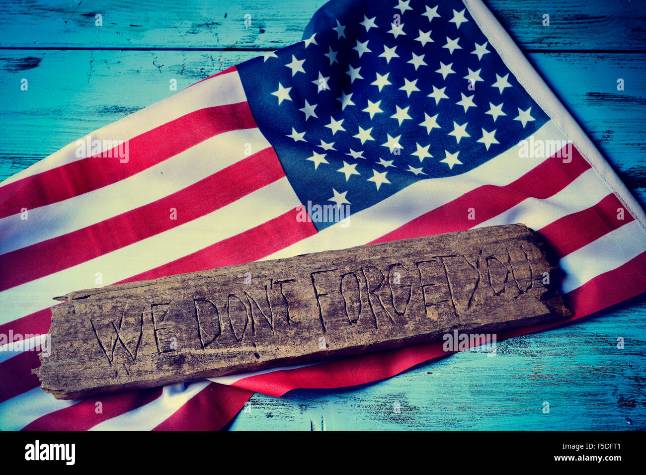 der Text, den wir nicht vergessen, dass Sie in ein Stück altes Holz und eine Flagge der Vereinigten Staaten, auf einem rustikalen blauen hölzernen Hintergrund geschnitzt Stockfoto