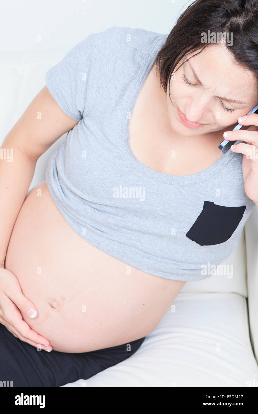 Schwangere Frau mit einem Telefon auf dem Sofa sitzen Stockfoto