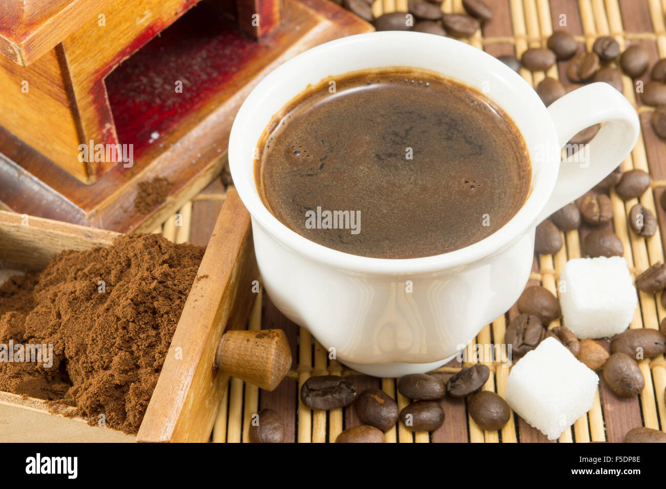 Tasse Kaffee mit Zucker und Kaffee Bohnen, neben gemahlenen Kaffee in einer Mühle-Schublade Stockfoto