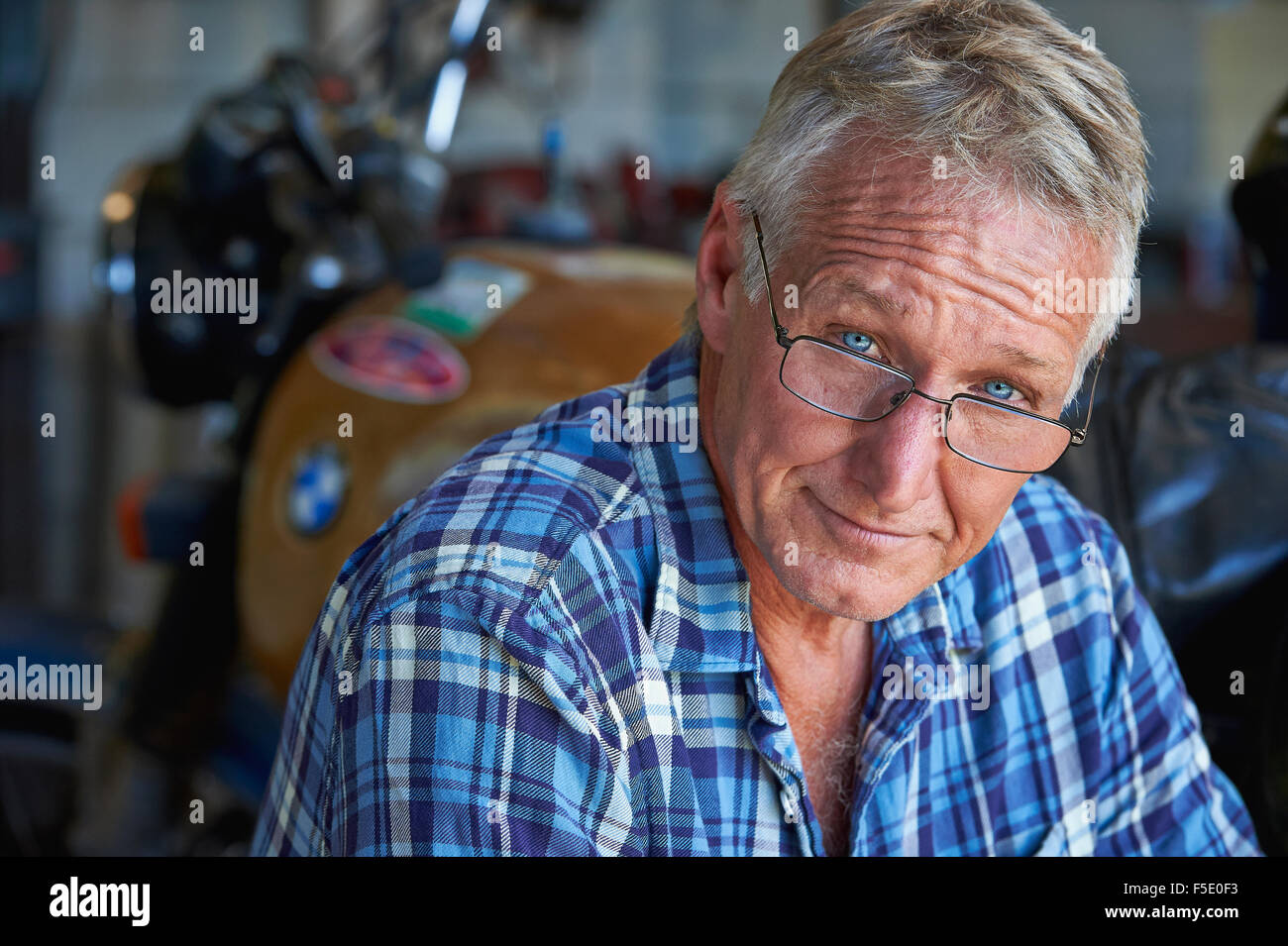 Porträt von einem nahen im Alter Mann und seinem alten Motorrad. Seine harte äußere wird durch seine blauen Augen und beruhigendes Lächeln gemildert. Stockfoto