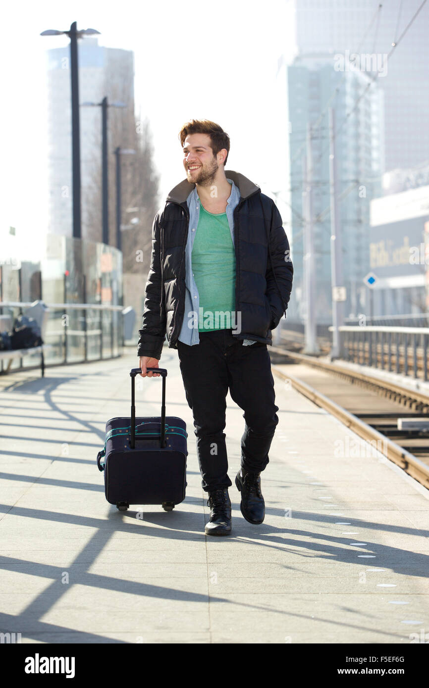 In voller Länge Portrait eines jungen Mannes mit Koffer am Bahnhof Bahnsteig lächelnd Stockfoto