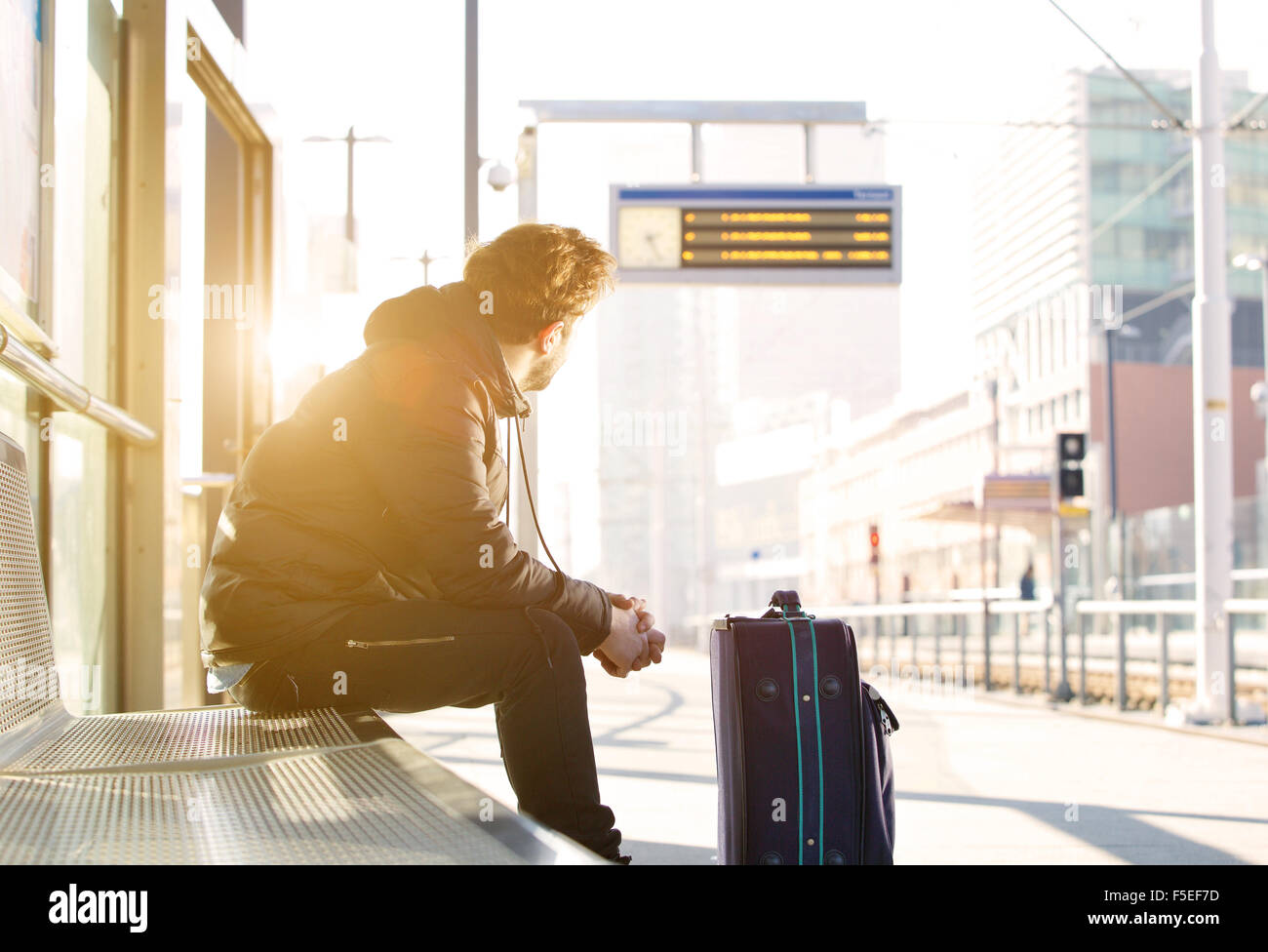 Porträt eines jungen Mannes sitzt am Bahnhof Blick auf Zeitplan Stockfoto