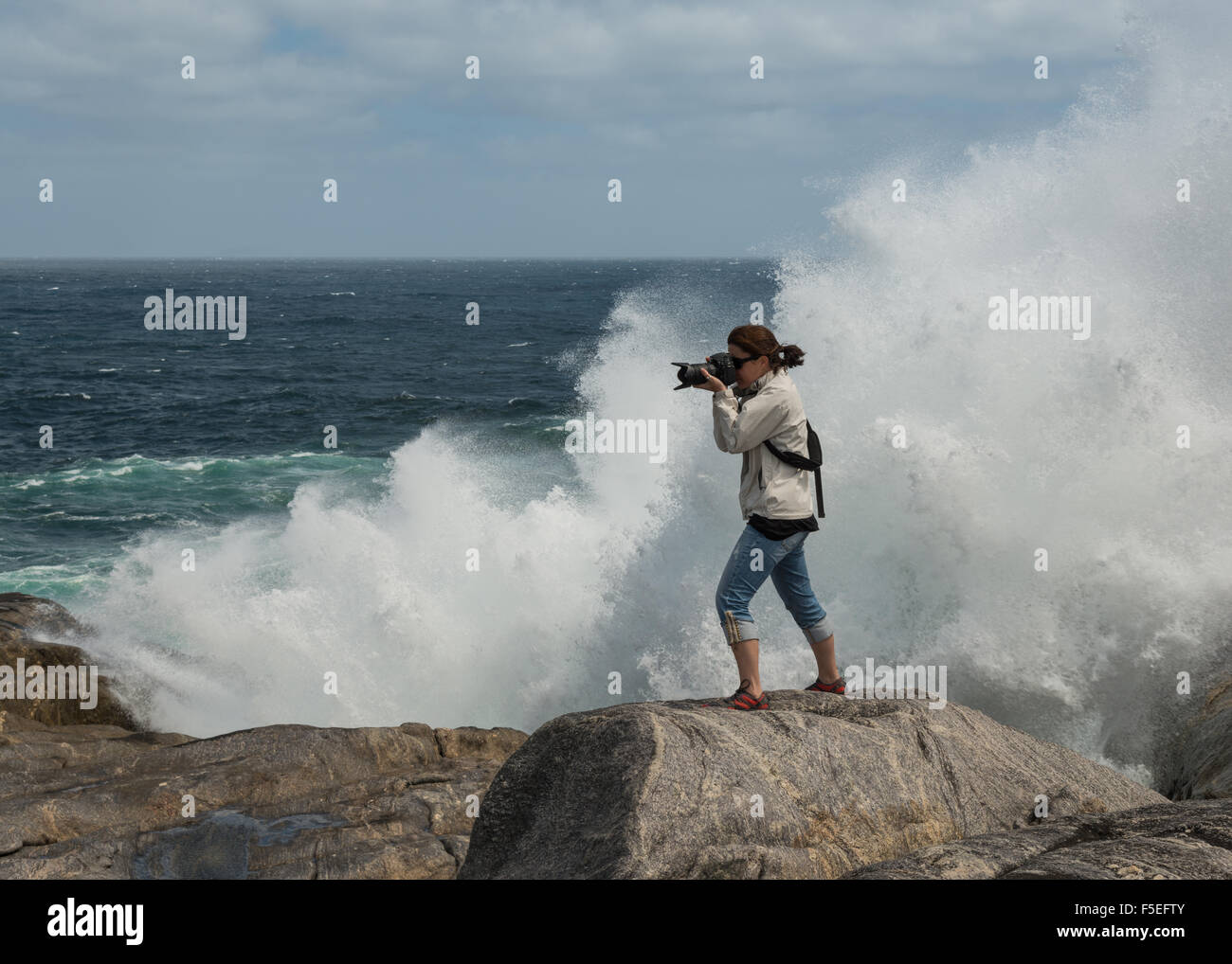 Frau, die auf den Felsen mit dem Fotografieren mit Wellen Stockfoto