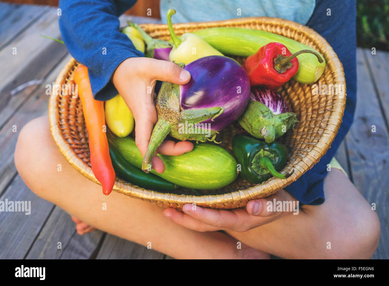 Junge mit einem Korb voller Gemüse Schneidersitz sitzen Stockfoto