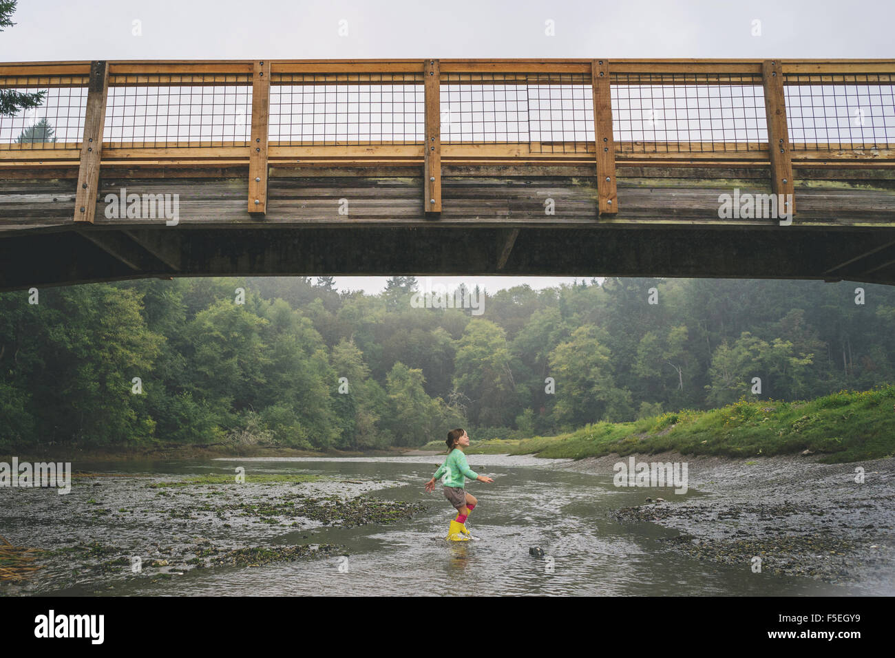 Mädchen spielen im flachen Wasser unter Brücke Stockfoto