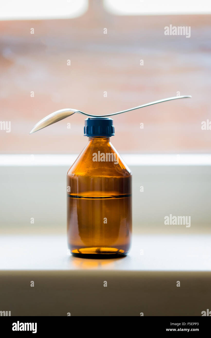 Eine Flasche Hustensaft mit einem Löffel in der Nähe des Fensters Stockfoto