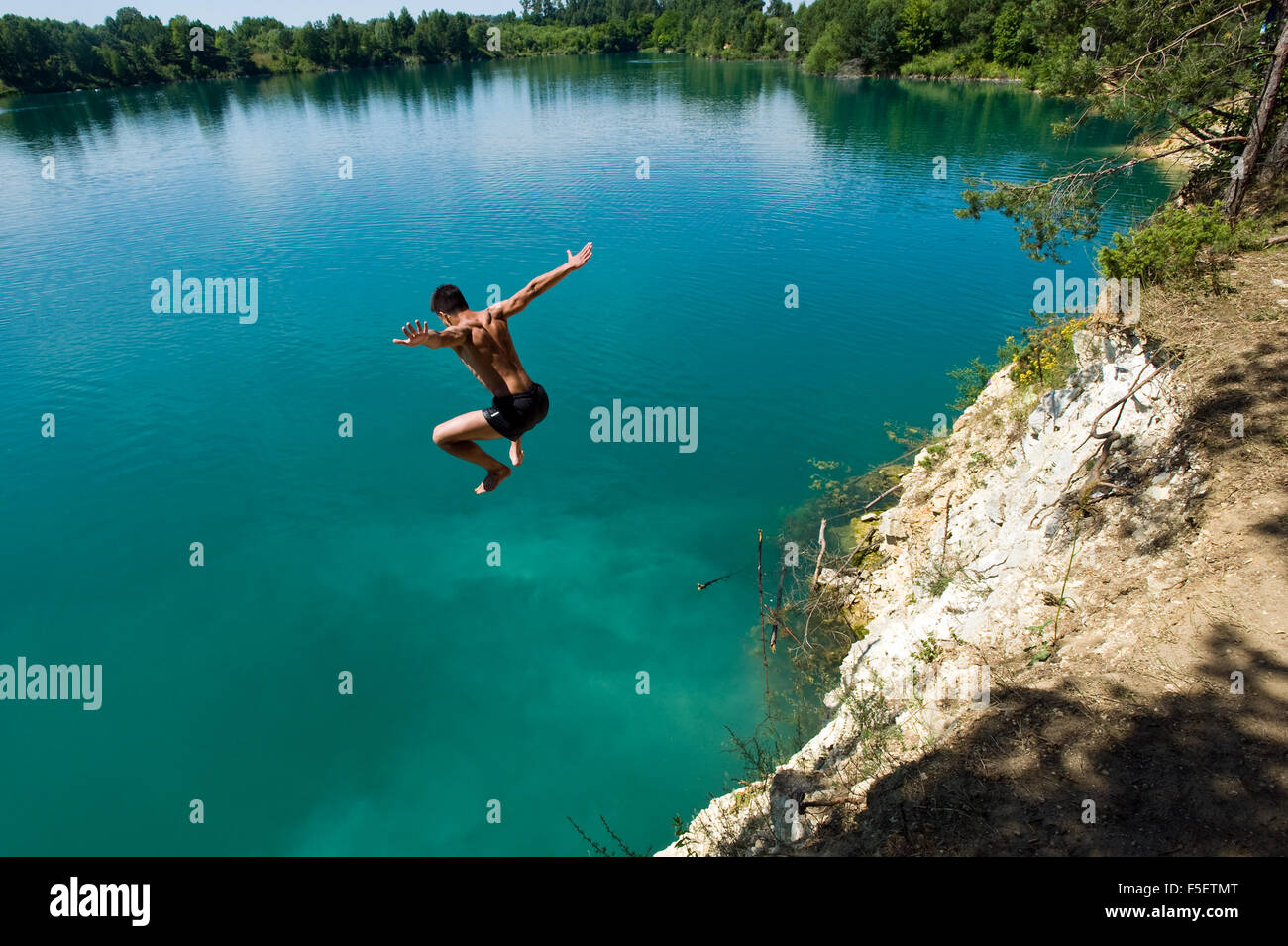 Junger Mann springt von der Klippe zu sauberem und türkisfarbenen Wasser in Sulejow. Polen. Stockfoto