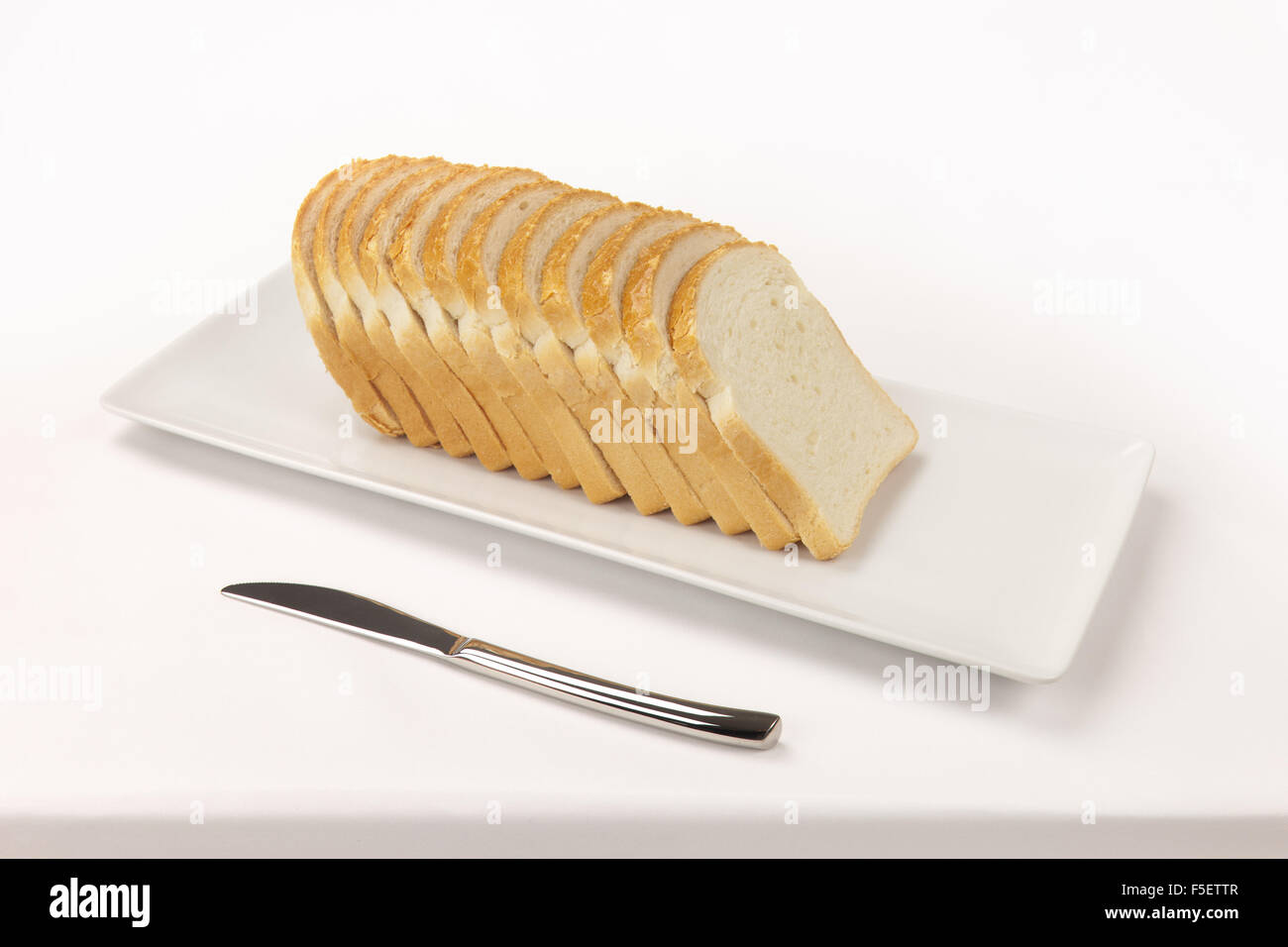 Geschnittenem Brot auf eine rechteckige Schale und ein Messer auf ein weißes Tischtuch. Stockfoto