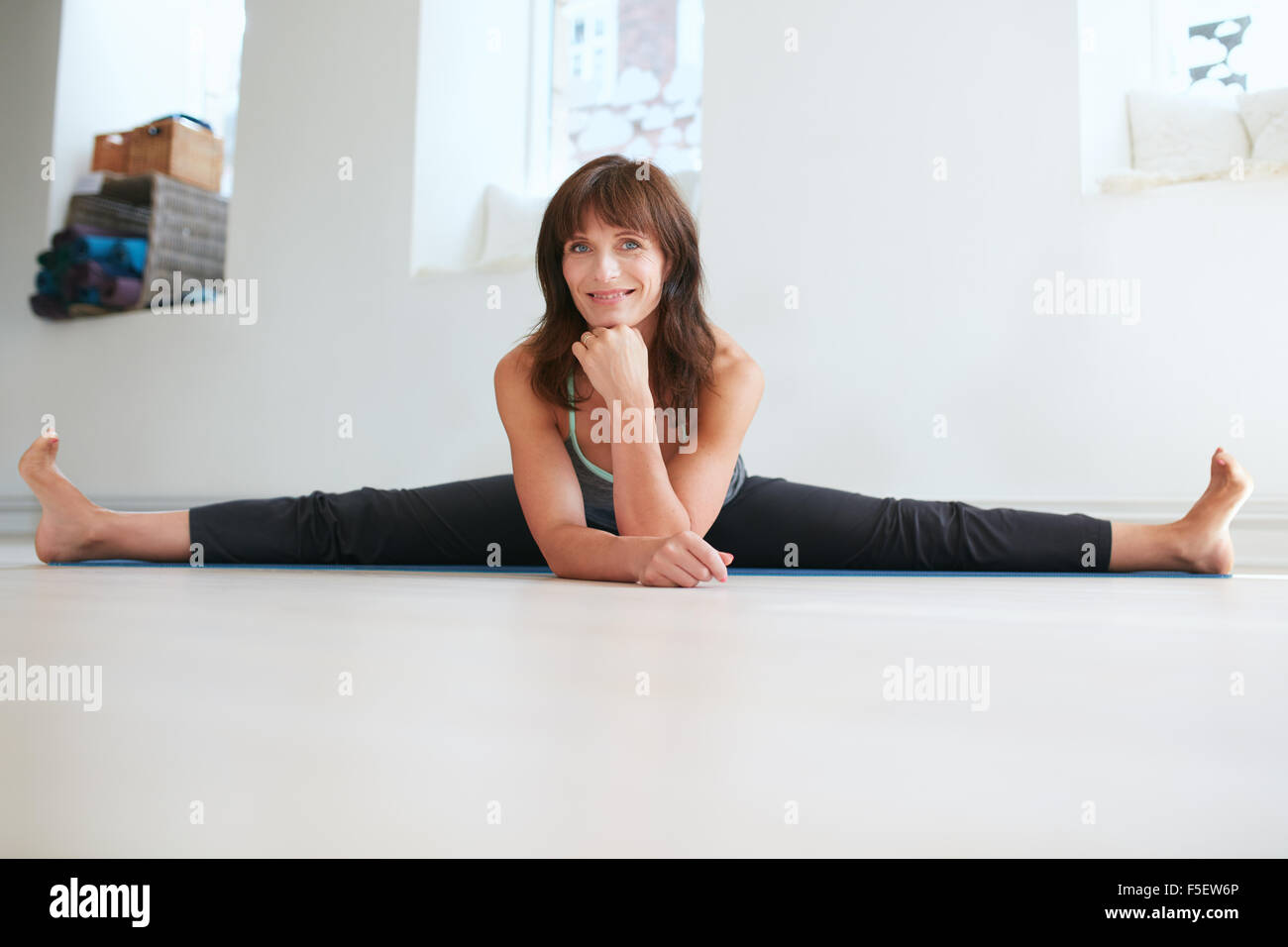 Foto von flexiblen Frau den Spagat zu tun. Hübsche Frau praktiziert Yoga im Fitness-Studio, Blick auf die Kamera zu Lächeln. Upavistha Konasana Stockfoto