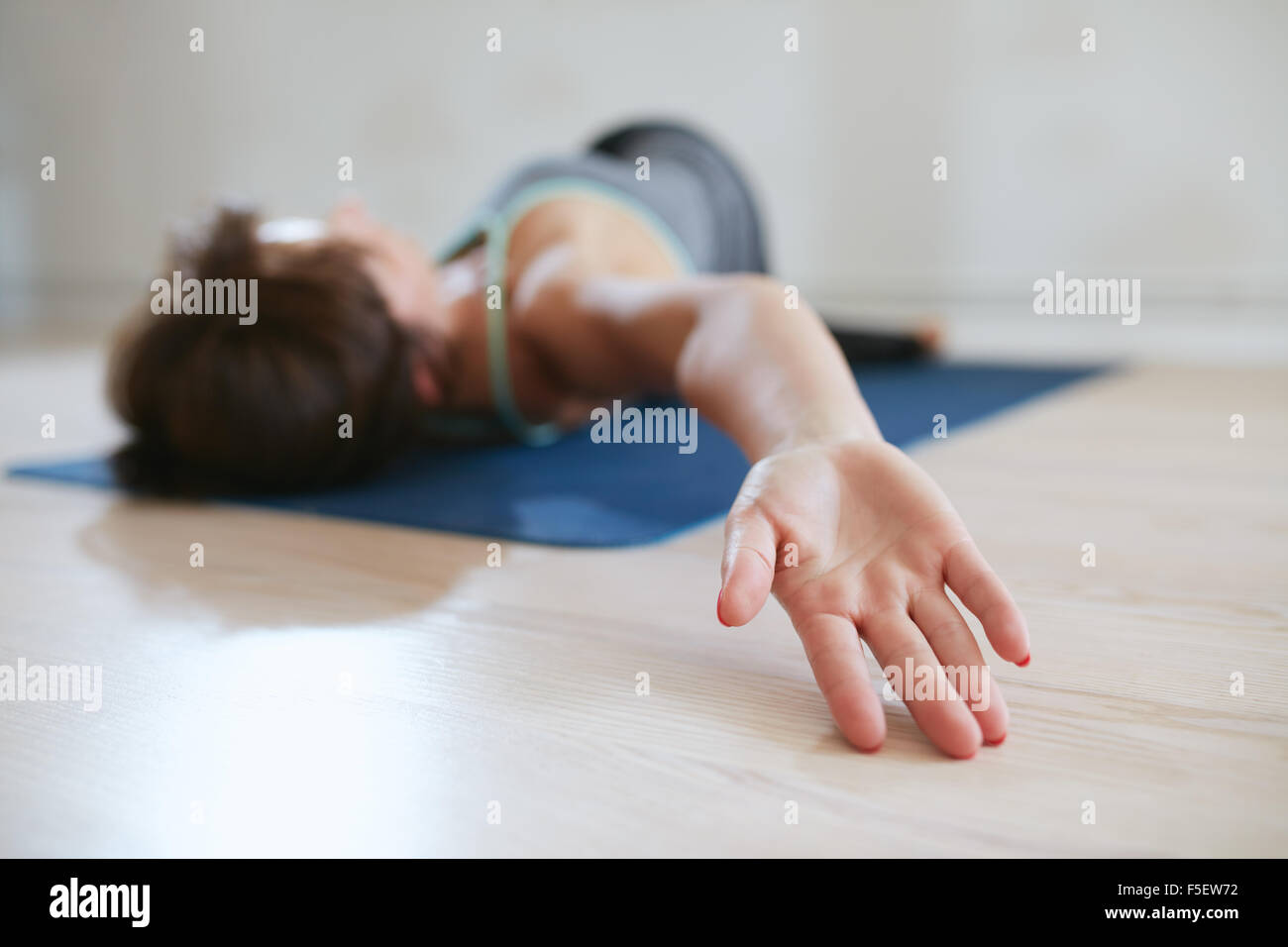 Frau erstreckt sich auf eine Gymnastikmatte, Fokus auf Seite. Frau am Boden drehen ihren Körper liegend. Stockfoto