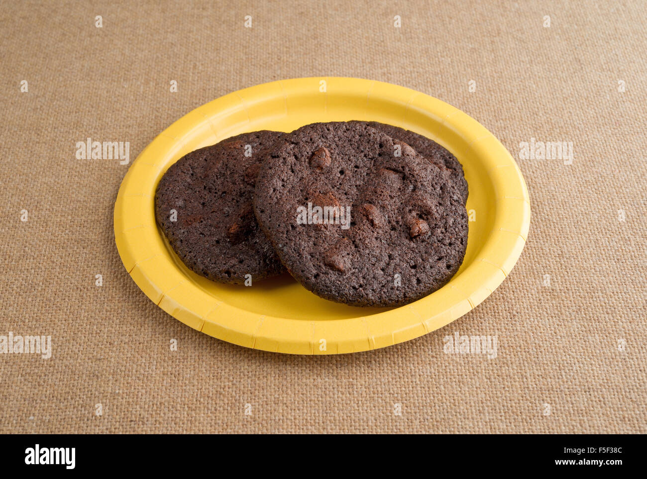 Drei gebackene frisch Schokoladenkekse knusprig Brownie auf eine gelbe Pappteller auf Sackleinen Tischdecke Stockfoto