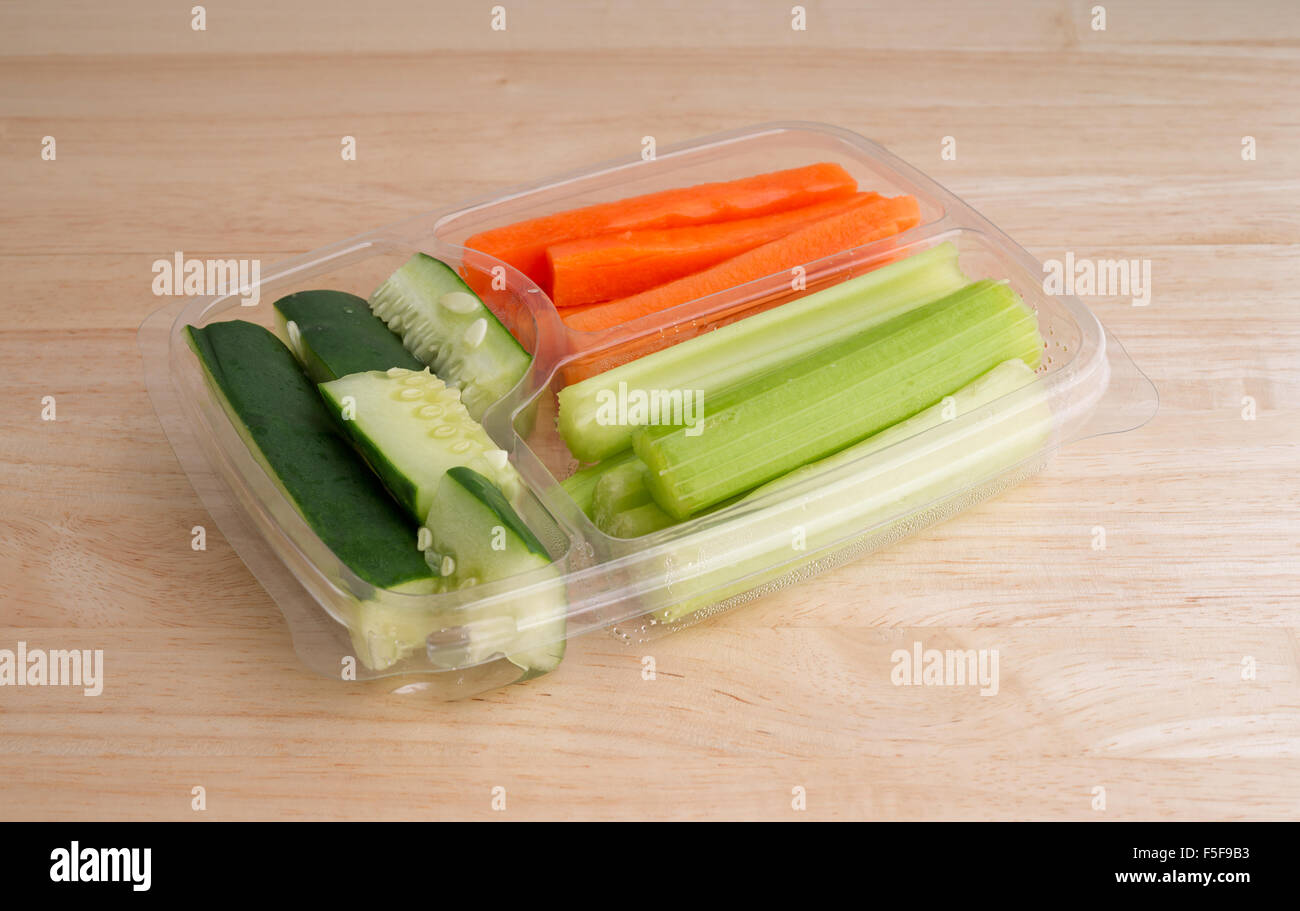 Snack-Gemüse mit Gurken Sellerie und Karotten in eine Plastikschale auf einem Holztisch mit natürlichem Licht beleuchtet. Stockfoto