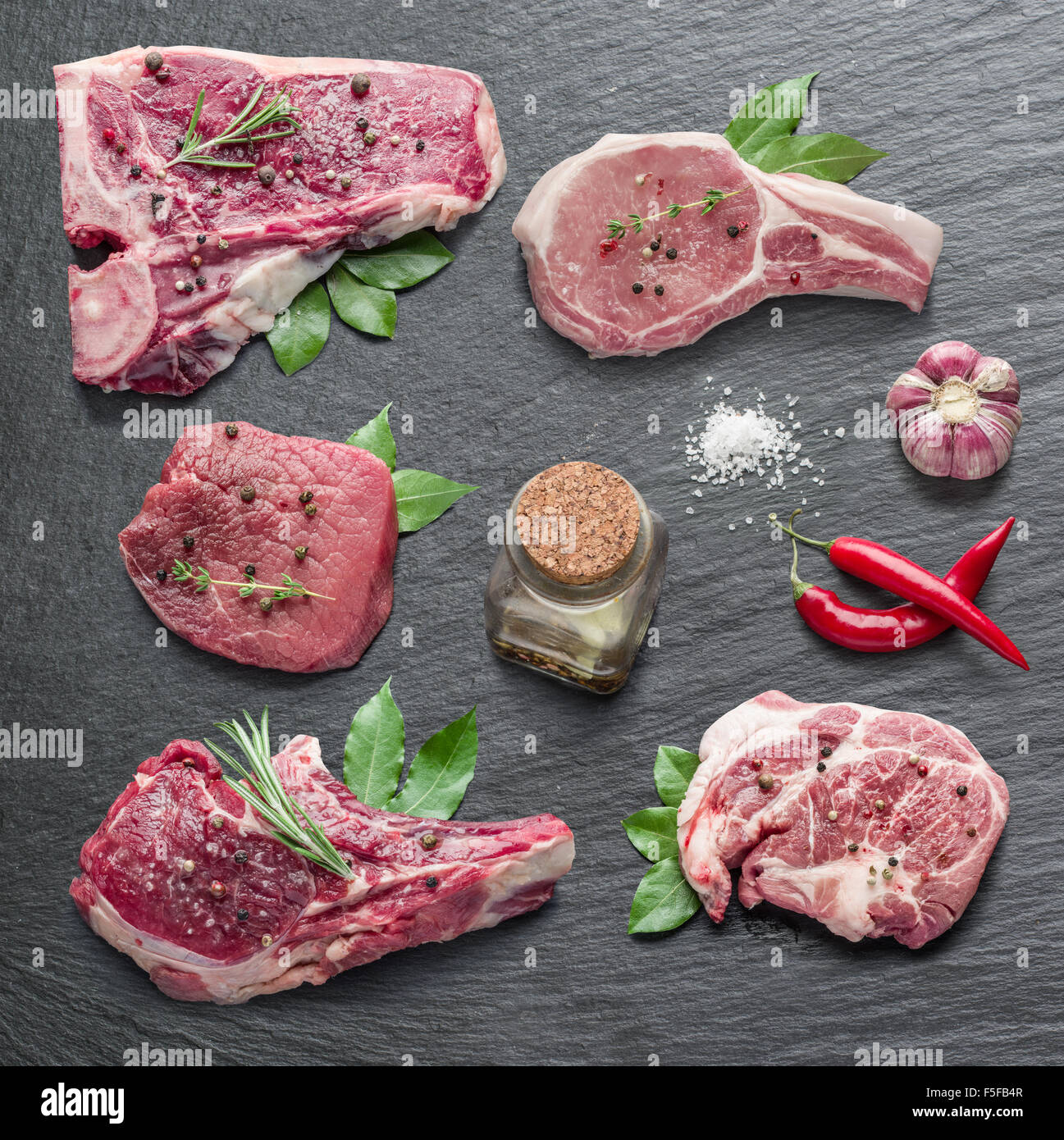 Rohes Fleisch Steaks mit Gewürzen auf dem schwarzen Schneidebrett. Stockfoto