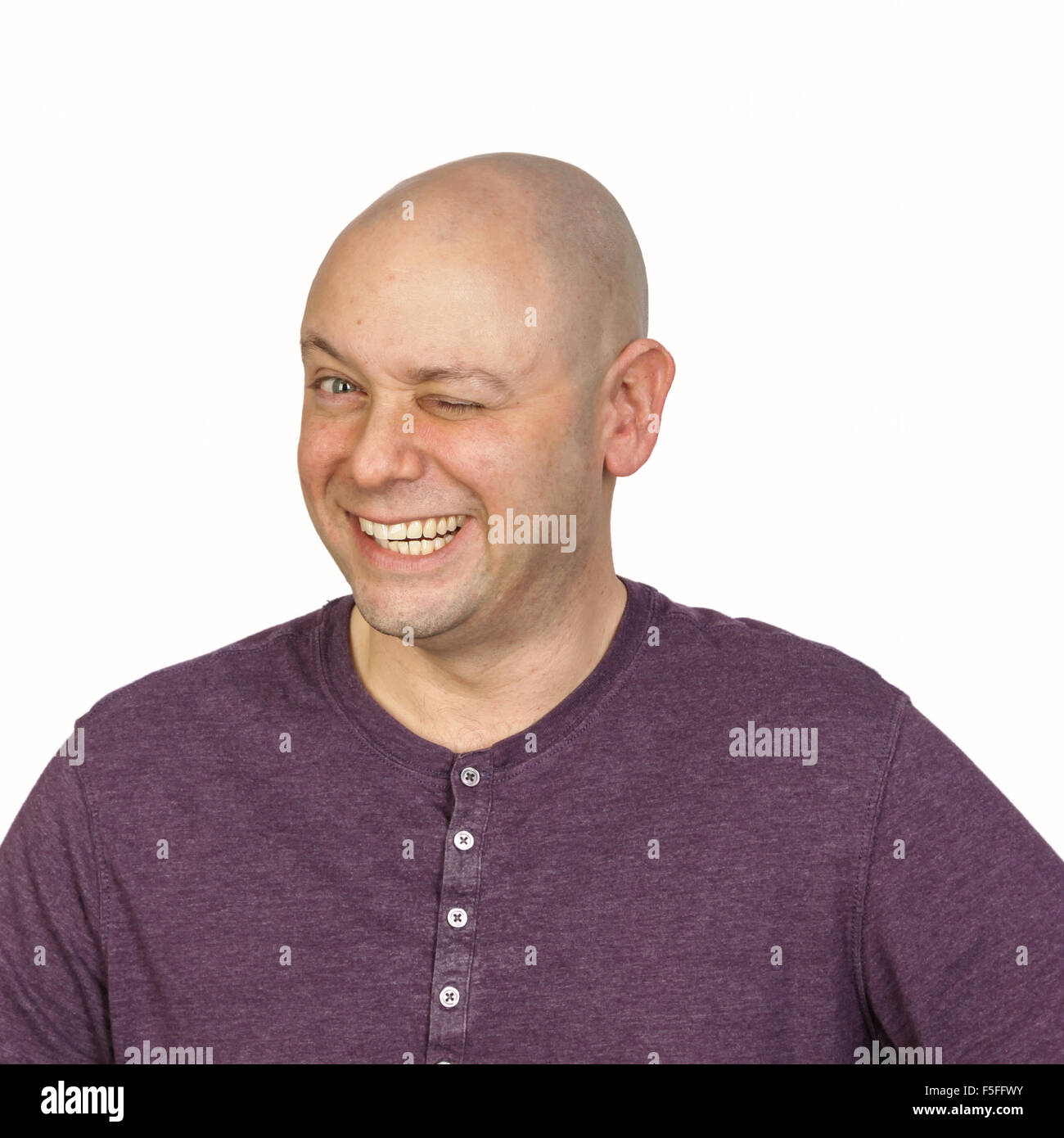 Big wink durch ein glatzköpfiger Mann im Studio auf weißem Hintergrund. Er trägt ein lila knöpfbare T-Shirt mit rundem Ausschnitt. Stockfoto
