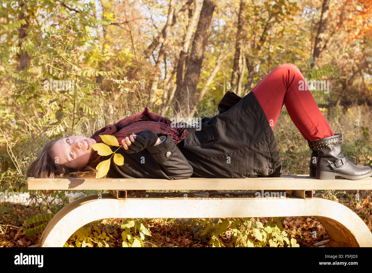 Schönes Mädchen auf der Bank liegen und halten im Herbst Blatt in einem Park in herbstlichen Farben gefärbt Stockfoto