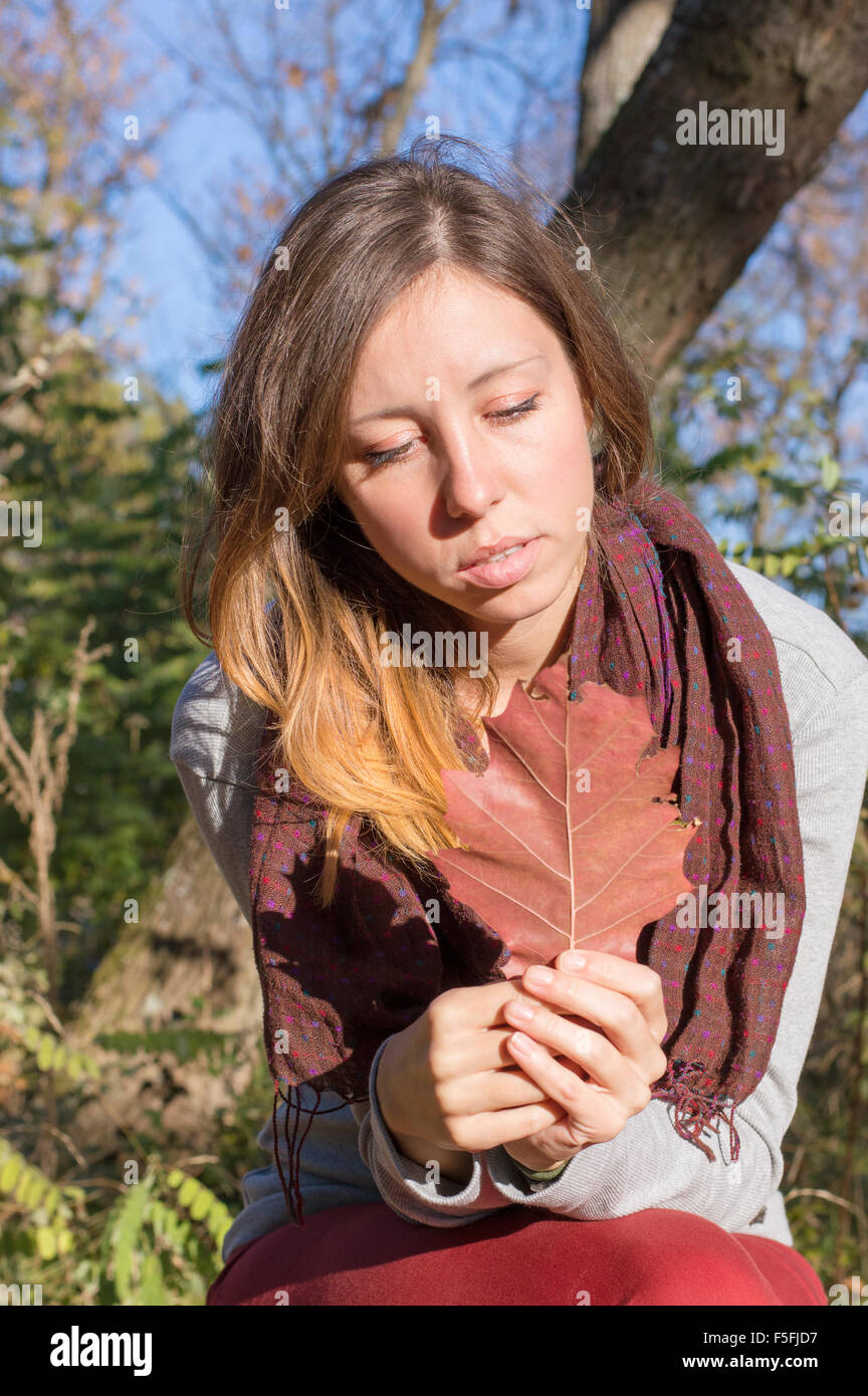 Trauriges Mädchen mit roten Herbst Blatt in der Hand beim Sitzen im park Stockfoto