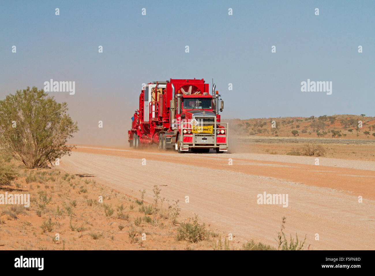 Lastzug, riesige rote Sattelauflieger / LKW beladen mit Bergbaumaschinen vor Staubwolke auf australischen outback Straße Stockfoto