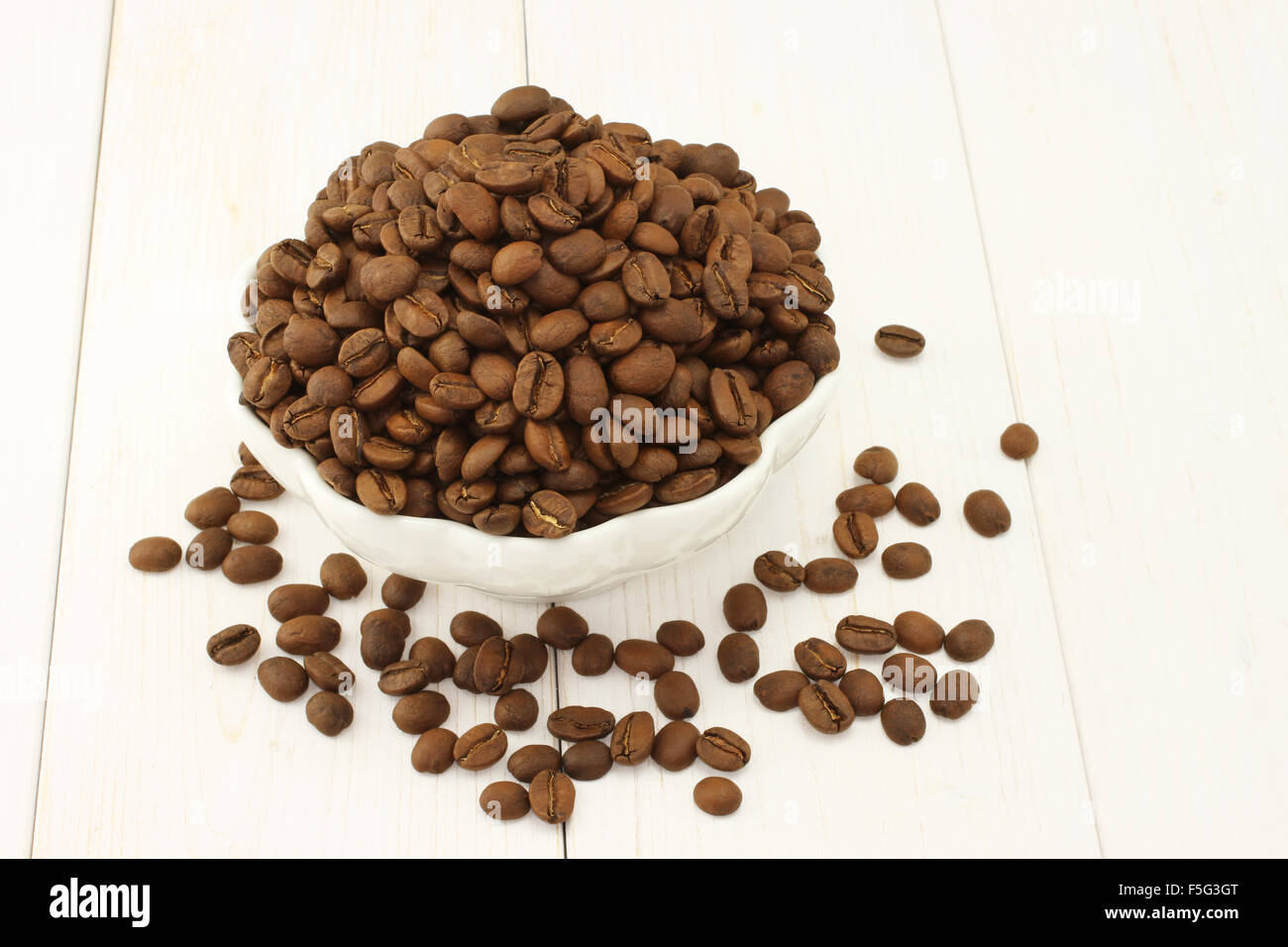 Geröstete Kaffeebohnen in weiße Schüssel und auf weißem Hintergrund aus Holz Stockfoto