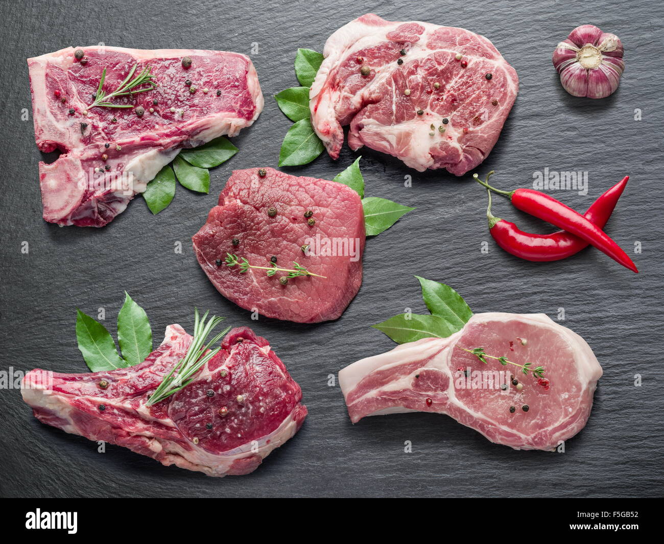 Rohes Fleisch Steaks mit Gewürzen auf dem schwarzen Schneidebrett. Stockfoto