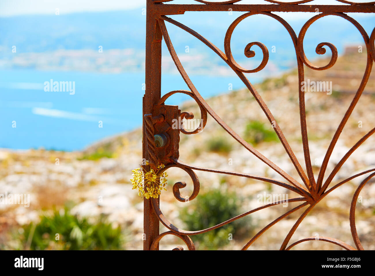 Mediterrane verrosteten Tor mit Meer im Hintergrund und wilden gelben Blüten Stockfoto