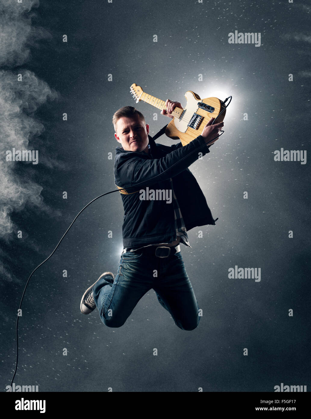 Rock und Roll-Gitarrist springt mit e-Gitarre mit Rauch und Pulver im Hintergrund Stockfoto