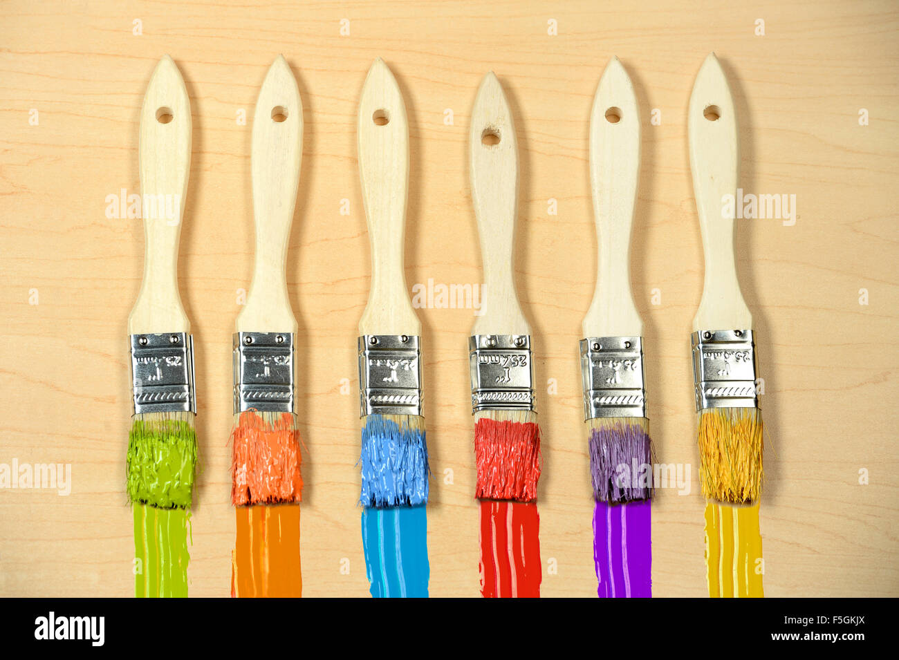 Sechs Pinsel mit Farbe in verschiedenen Farben über Holz Stockfoto