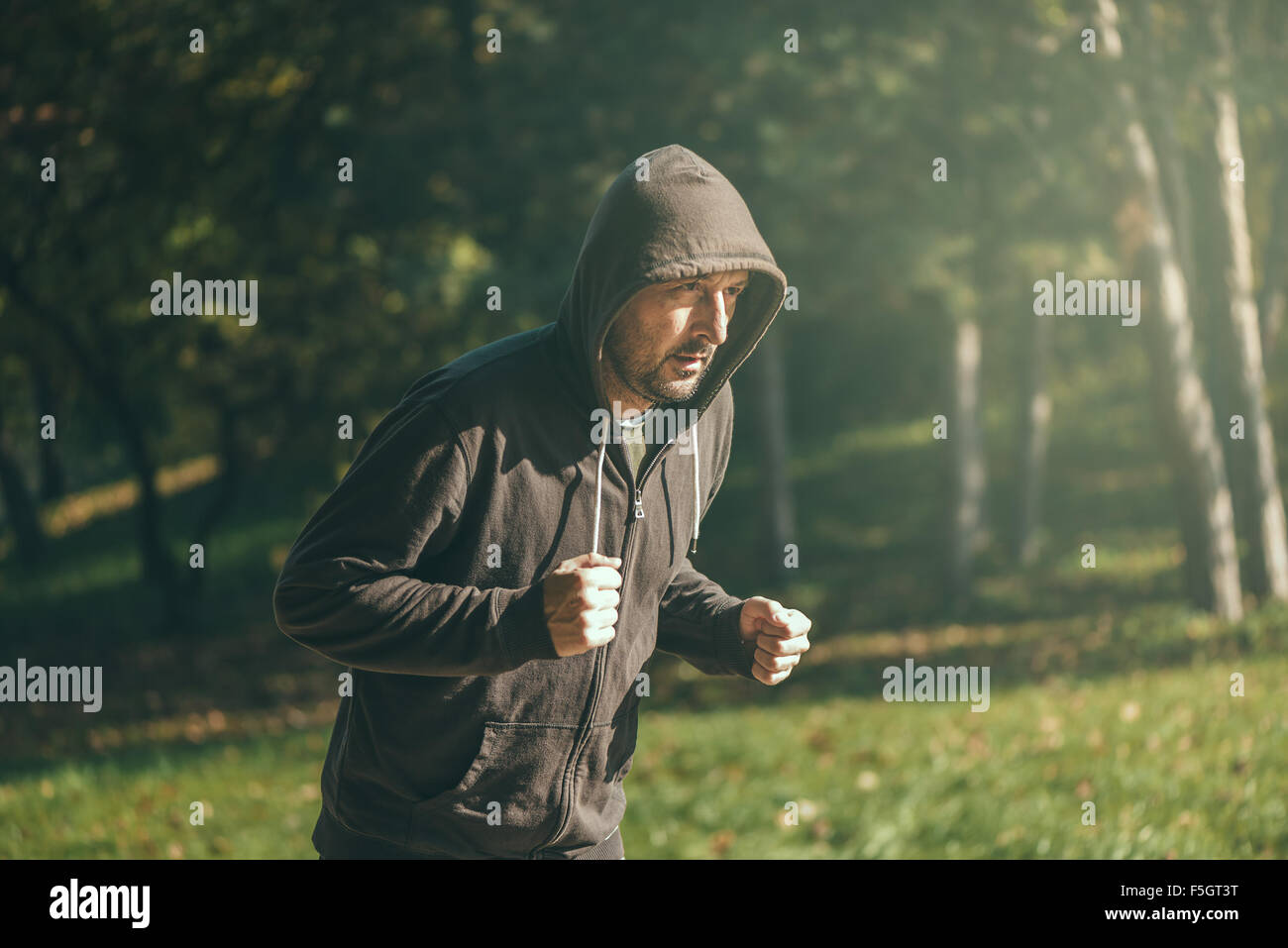 Vermummte Mann Joggen im Park im frühen Herbstmorgen, Sport, Erholung und gesunden Lifestyle-Konzept, Retro-getönten Bild mit Stockfoto