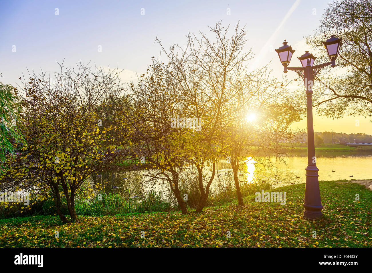 Herbst-Landschaft mit Straßenbeleuchtung in der Nähe von See bei Sonnenuntergang Stockfoto