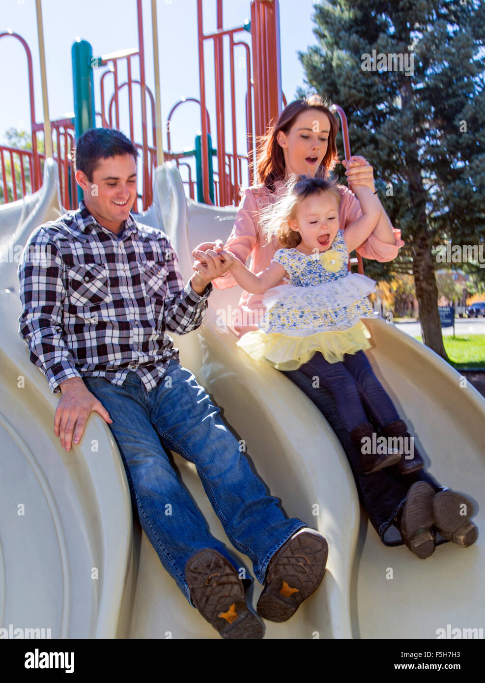 Vater, Mutter und niedliche junge Tochter spielen auf Park Schiebe-board Stockfoto