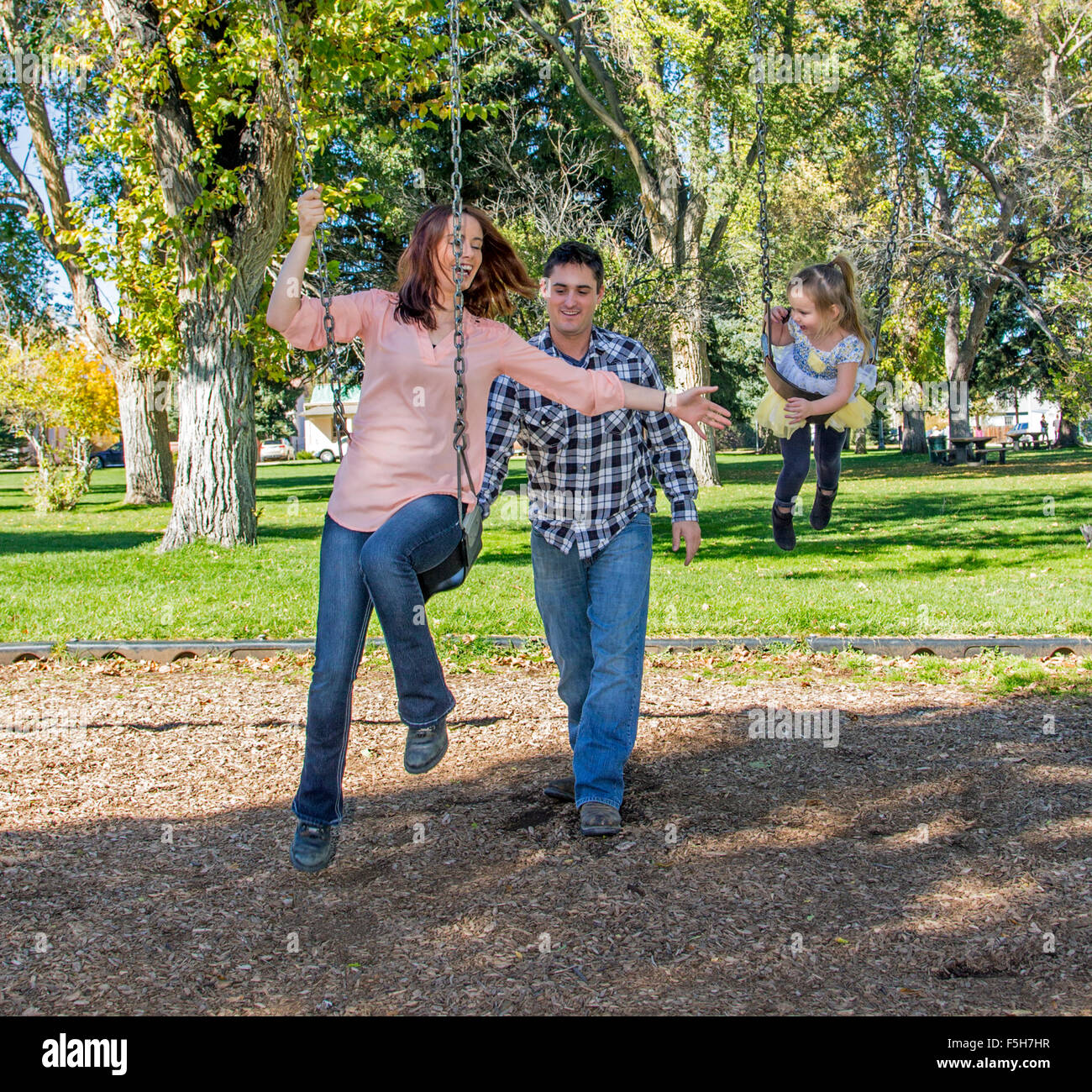 Vater, Mutter und niedliche kleine Tochter spielen auf Park schwingt Stockfoto