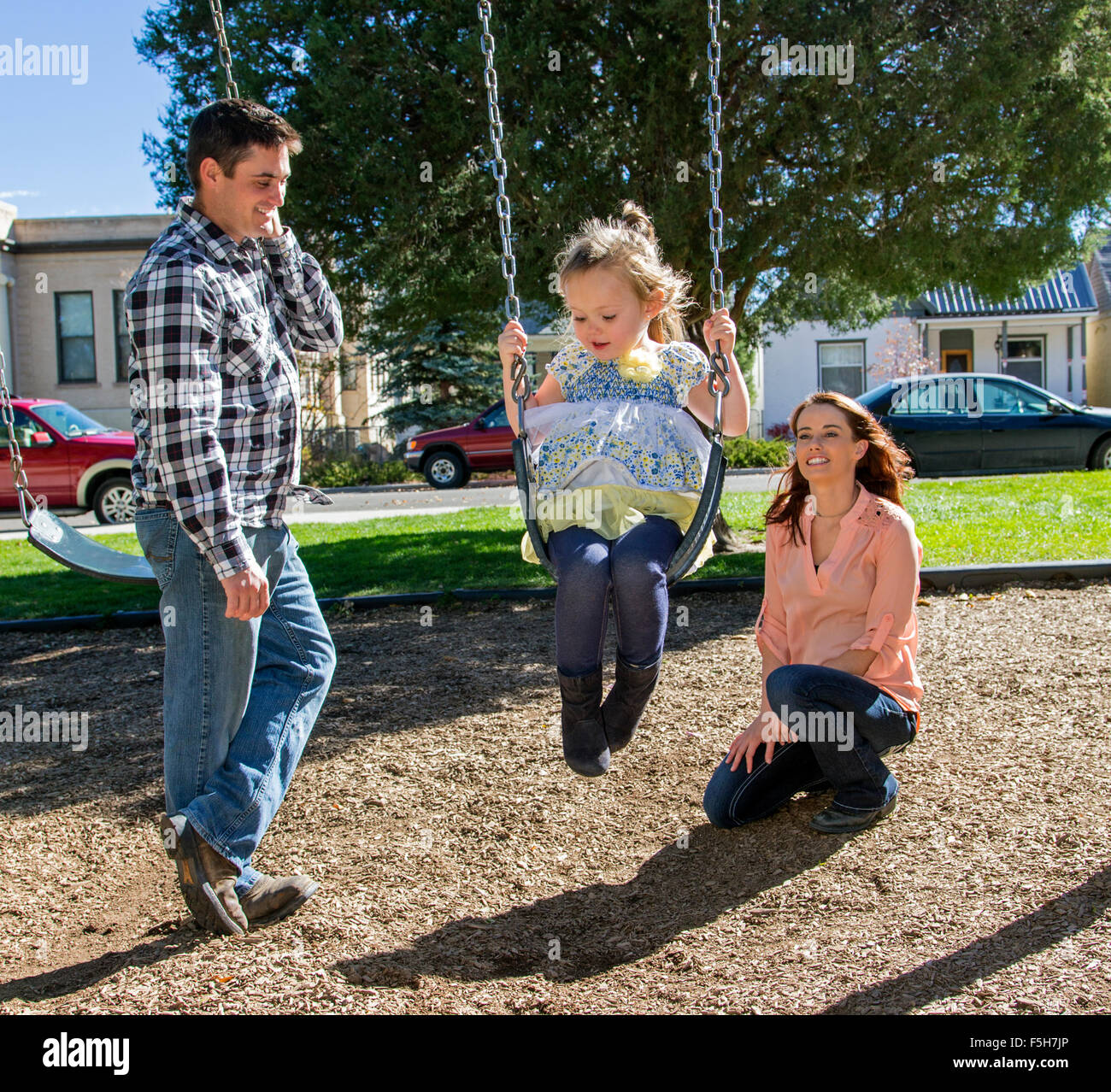 Vater, Mutter und niedliche kleine Tochter spielen auf Park schwingt Stockfoto