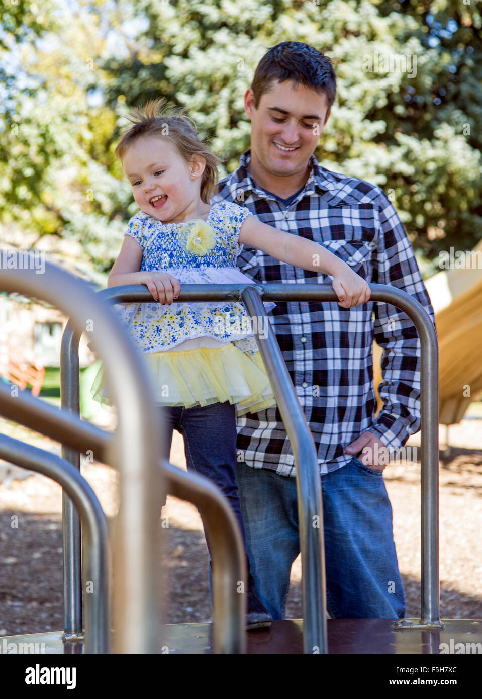 Vater und junge Tochter auf einem Karussell, sonnigen Tag, Park Spielplatz draußen spielen Stockfoto