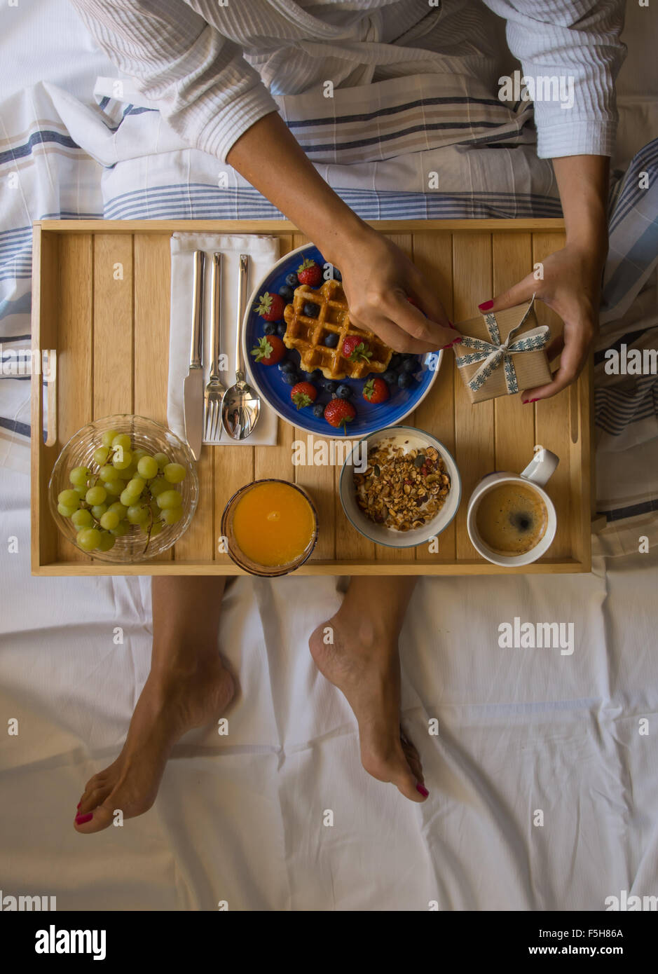 Frau mit Frühstück im Bett auf einem Holztablett Stockfoto