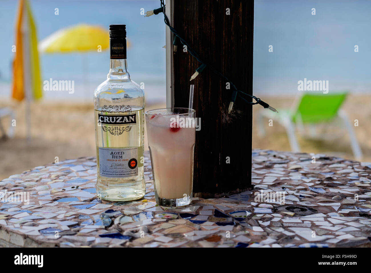 Eine Flasche Cruzan im Alter Rum und einen cocktail in ein Glas mit einem Sonnenschirm und das Karibische Meer im Hintergrund Rum. Stockfoto